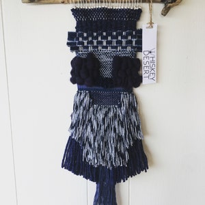 Puede incluir: Un tapiz tejido de pared azul y blanco con un borde de flecos y una etiqueta que dice "Whiskey Desert".