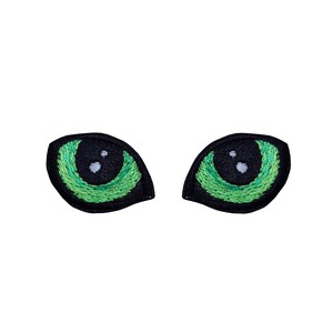 May include: Two green embroidered eyes with black pupils and white highlights. The eyes are on a white background.