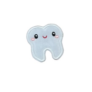 May include: A light blue embroidered patch shaped like a tooth with a smiling face. The tooth has black eyes, red lips, and pink cheeks.