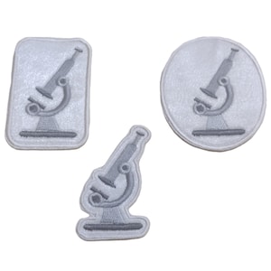 May include: Three grey microscope patches in various shapes: rectangular, oval, and a freeform design. Each patch features a detailed embroidered microscope, ideal for science enthusiasts or craft projects.