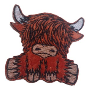 May include: An embroidered patch of a Highland cow with a fluffy mane, sitting with its legs crossed. The patch is brown and black.