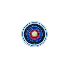 May include: Circular embroidered patch with a target design. The patch features concentric circles in blue, red, black, and yellow, with a light blue border. The patch has a stitched appearance and is designed to be sewn onto fabric.
