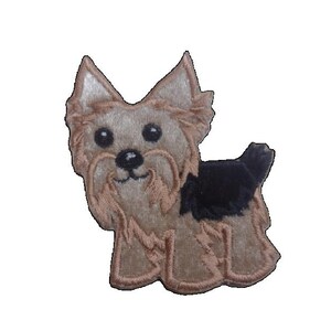 May include: An embroidered patch featuring a stylised Yorkshire Terrier dog. The design showcases the dog's tan and black fur, pointed ears, and dark eyes. The edges of the patch are finished with a tan thread border, creating a distinct outline.