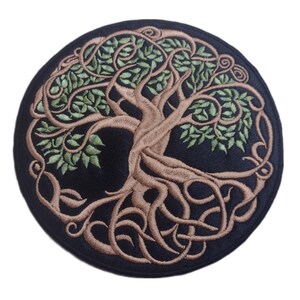 May include: Circular black patch with an embroidered tree design. The tree features a brown trunk and roots, and green leaves. The design is framed by a decorative border. Suitable for clothing or accessories.