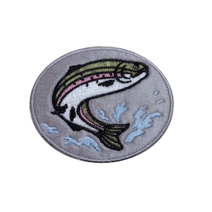 May include: A grey embroidered patch featuring a white and green fish leaping from the water. The fish has pink stripes and is surrounded by blue water.