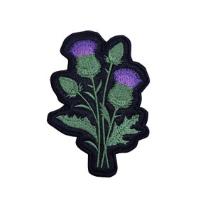 May include: A black embroidered patch featuring a bouquet of three purple and green thistles.