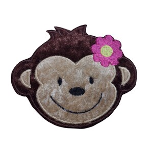 May include: Brown felt monkey face with a pink flower with a yellow centre. The monkey has a brown nose and a big smile.