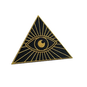 May include: A black and gold embroidered patch featuring an eye within a triangle, a symbol often associated with the concept of the all-seeing eye. The patch has a detailed design with radiating lines and a gold eye.