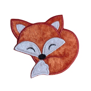 May include: A plush orange fox applique with white eyes and a black nose. The fox is curled up in a sleeping position.