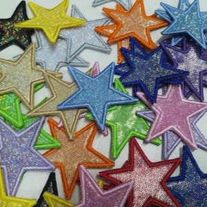 May include: A selection of star-shaped patches in a variety of colours. The patches have a glittery, textured finish and are outlined with a contrasting colour. The colours include blue, green, orange, and pink, creating a bright and appealing design.
