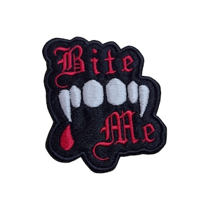 May include: Embroidered patch with a black background and a stylized design. The patch features white teeth and fangs, with the words "Bite Me" in red gothic lettering. A red drop of blood is also present.