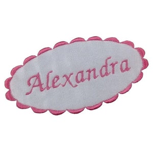 May include: White oval fabric patch with a pink scalloped edge. The name "Alexandra" is embroidered in pink cursive lettering.