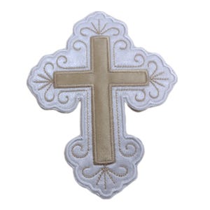 May include: A white embroidered cross with a gold cross in the centre. The cross has a decorative design around the edges.