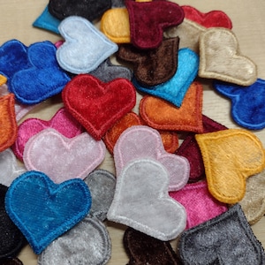 May include: A collection of felt heart patches in various colours, including red, blue, pink, orange, and brown. The hearts are all different sizes and shapes, and some have a slightly raised texture.