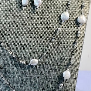 May include: A silver chain necklace with white pearls and black beads. The necklace is layered and has a matching pair of earrings with white pearls and black beads.