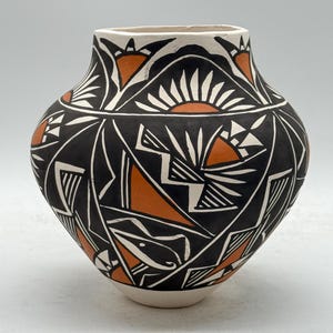 Könnte beinhalten: Eine handgefertigte Keramikvase mit breitem Körper und schmalem Hals. Die Vase hat einen schwarzen Hintergrund mit geometrischen Designs in Weiß und Orange. Der Rand und der Boden sind weiß. Das Design umfasst Dreiecke, Linien und sonnenartige Formen.