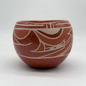 以下が含まれることがあります： 白の幾何学模様が施された、テラコッタ色の小さくて丸い陶器のボウル。ボウルは口が広く、底が丸みを帯びています。デザインは曲線と形が特徴で、ユニークなパターンを作り出しています。ボウルはおそらく手作りです。