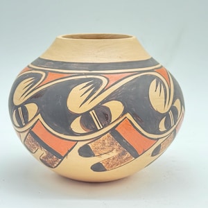 May include: A round ceramic pot with a wide, short neck and a matte tan base. The exterior features a repeating hand-painted pattern of black and orange curved shapes, with textured brown accents integrated into the geometric design.