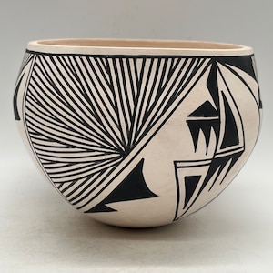 Peut inclure: Un bol en céramique blanche avec des motifs géométriques noirs. Le bol a une forme arrondie et un bord large.