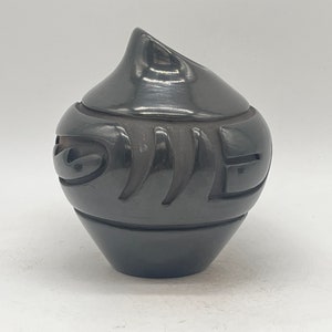 May include: Black pottery jar with a carved design. The jar has a rounded body and a pointed lid.