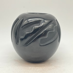 May include: A black ceramic pot with a geometric design. The pot is round and has a smooth, glossy finish.