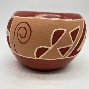 May include: A small, round, terracotta pot with a brown and white geometric design. The pot has a wide mouth and a rounded bottom.