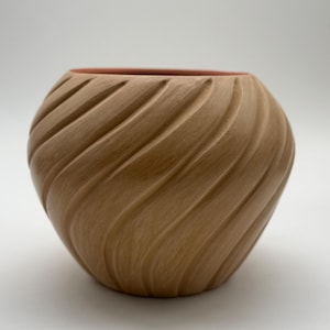 May include: A rounded ceramic planter with a light brown exterior featuring diagonal, swirling carved grooves. The interior of the vessel is finished in a contrasting salmon-pink colour, visible at the circular opening of the pot.
