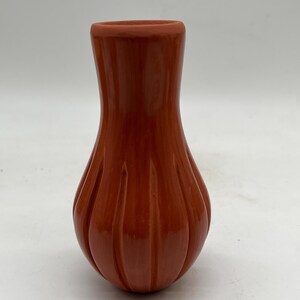 May include: A small, terracotta-coloured pottery vase with a ribbed design. The vase has a rounded bottom and a narrow neck.