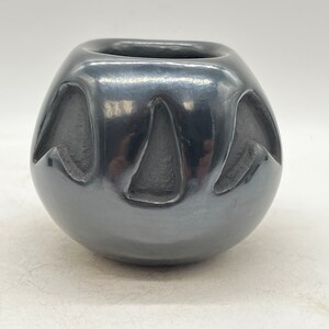 May include: A black ceramic pot with a smooth, shiny finish. The pot has a rounded shape and features a carved design of three stylized birds.