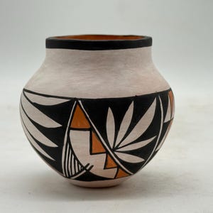 May include: A handcrafted pottery vase with a rounded body and a wide opening. The vase features a cream-colored exterior with a black band of geometric and leaf-like designs. Orange accents are incorporated into the design. The rim is black.