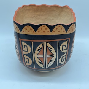 May include: A black and orange ceramic bowl with a geometric design. The bowl has a scalloped rim and is decorated with a repeating pattern of diamonds and swirls.