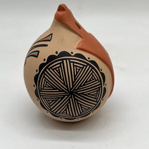 Może przedstawiać: Ręcznie malowana ceramiczna figurka ptaka w kolorze beżowym. Ptak ma geometryczny czarno-biały wzór na ciele, z pomarańczowymi akcentami na dziobie i głowie. Figurka ma zaokrąglony korpus i spiczasty dziób.