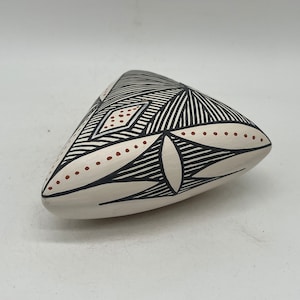 May include: A white triangular ceramic sculpture with black and red geometric designs. The sculpture has a smooth, matte finish.