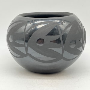 以下が含まれることがあります： 黒い陶器のボウルで、幾何学模様が施されています。ボウルは、黒い線と円形の模様で飾られています。