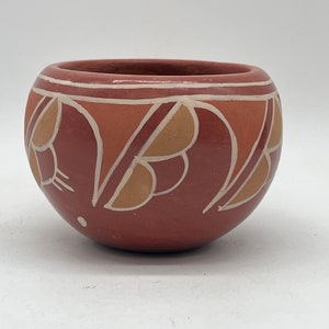以下が含まれることがあります： テラコッタ色の小さな丸い陶器のボウル。ボウルには、白で縁取られた、ベージュとオレンジの色合いの、様式化された葉の形が繰り返されるデザインが施されています。白い帯が縁を囲んでいます。