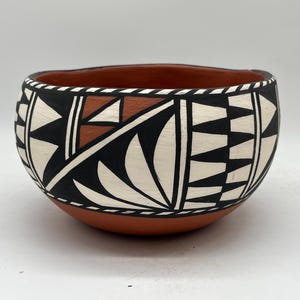 May include: Handmade ceramic bowl with a terracotta base and interior. The exterior features a geometric pattern in black, white, and brown. The bowl's design showcases traditional Native American pottery techniques.