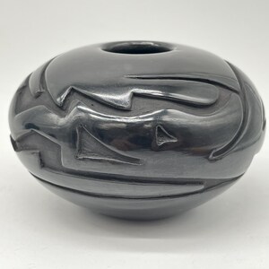 May include: Black pottery bowl with a geometric design. The bowl is made by a Native American artist and is a beautiful example of traditional pottery.