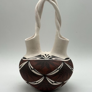 May include: A ceramic vessel with two spouts connected by a single twisted handle. The lower body features a dark brown and black geometric pattern with fine line work, while the upper spouts and handle are a smooth, matte off-white finish.