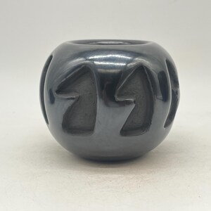 May include: Black pottery bowl with a geometric design. The bowl is round and has a smooth, glossy finish.