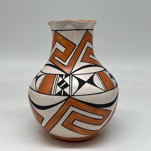 Può includere: Un vaso in ceramica dipinto a mano con base color crema, ornato con motivi geometrici arancioni, neri e bianchi. Il vaso ha un corpo arrotondato e un bordo leggermente svasato e smerlato. Il design presenta forme e linee angolari.