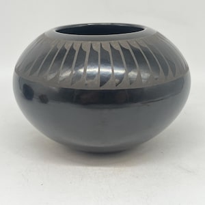 May include: Black pottery bowl with a geometric design. The bowl has a wide rim and a rounded base.