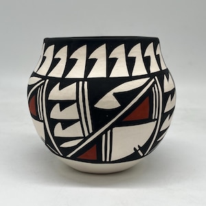 Może przedstawiać: Ręcznie malowany ceramiczny garnek z czarną obwódką i geometrycznymi wzorami w kolorze czarnym, białym i czerwonym. Garnek ma zaokrąglony kształt i kremową podstawę, prezentując tradycyjną sztukę rdzennych Amerykanów.