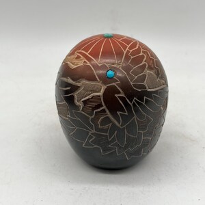 May include: A hand-carved, black pottery gourd with a bird design and turquoise accents. The gourd is decorated with intricate carvings and has a smooth, polished finish.