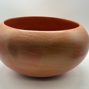 May include: A round, terracotta-colored ceramic bowl with a wide opening. The bowl has a smooth, rounded shape and a textured surface. The interior is a darker shade of the same color. This decorative bowl is suitable for home decor.