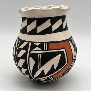 Puede incluir: Una olla de cerámica blanca con un borde festoneado, decorada con patrones geométricos negros y naranja. La olla es de estilo tradicional nativo americano.