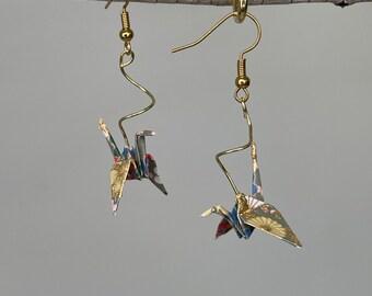 May include: Gold origami crane earrings with a colorful patterned paper design. The earrings are hanging from a branch.