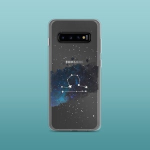 Peut inclure: Une coque de t&eacute;l&eacute;phone transparente avec un imprim&eacute; galaxie et la constellation de la Balance en blanc. La coque porte l'inscription "SAMSUNG" au dos.
