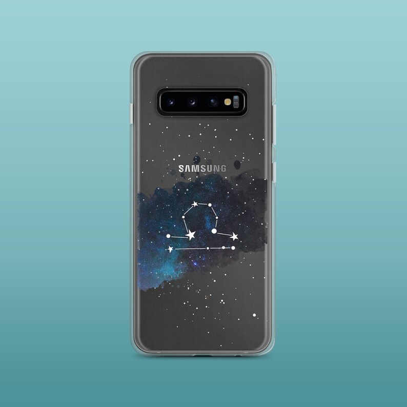 Peut inclure: Une coque de t&eacute;l&eacute;phone transparente avec un imprim&eacute; galaxie et la constellation de la Balance en blanc. La coque porte l'inscription "SAMSUNG" au dos.