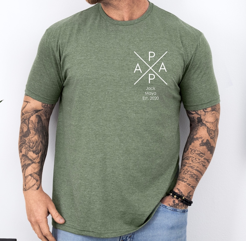 Puede incluir: Una camiseta verde con un dise&ntilde;o gr&aacute;fico blanco. El gr&aacute;fico presenta una cruz con las letras "PAPA" y el texto "Jack Maya Est. 2020".
