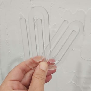 May include: Three clear plastic sewing pattern templates in the shape of an oval with a rounded edge. The templates are stacked on top of each other.